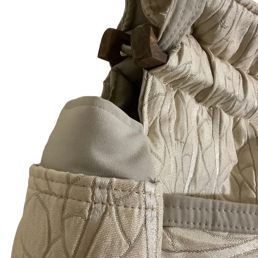 FABRIC SHOULDER BAG WITH OUTSIDE SURROUNDING POCKETS IN A CREAM AND TAUPE COLOR.